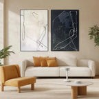 Minimalist Abstract Duo: black and white line art paintings in black frames above cream sofa with mustard pillows