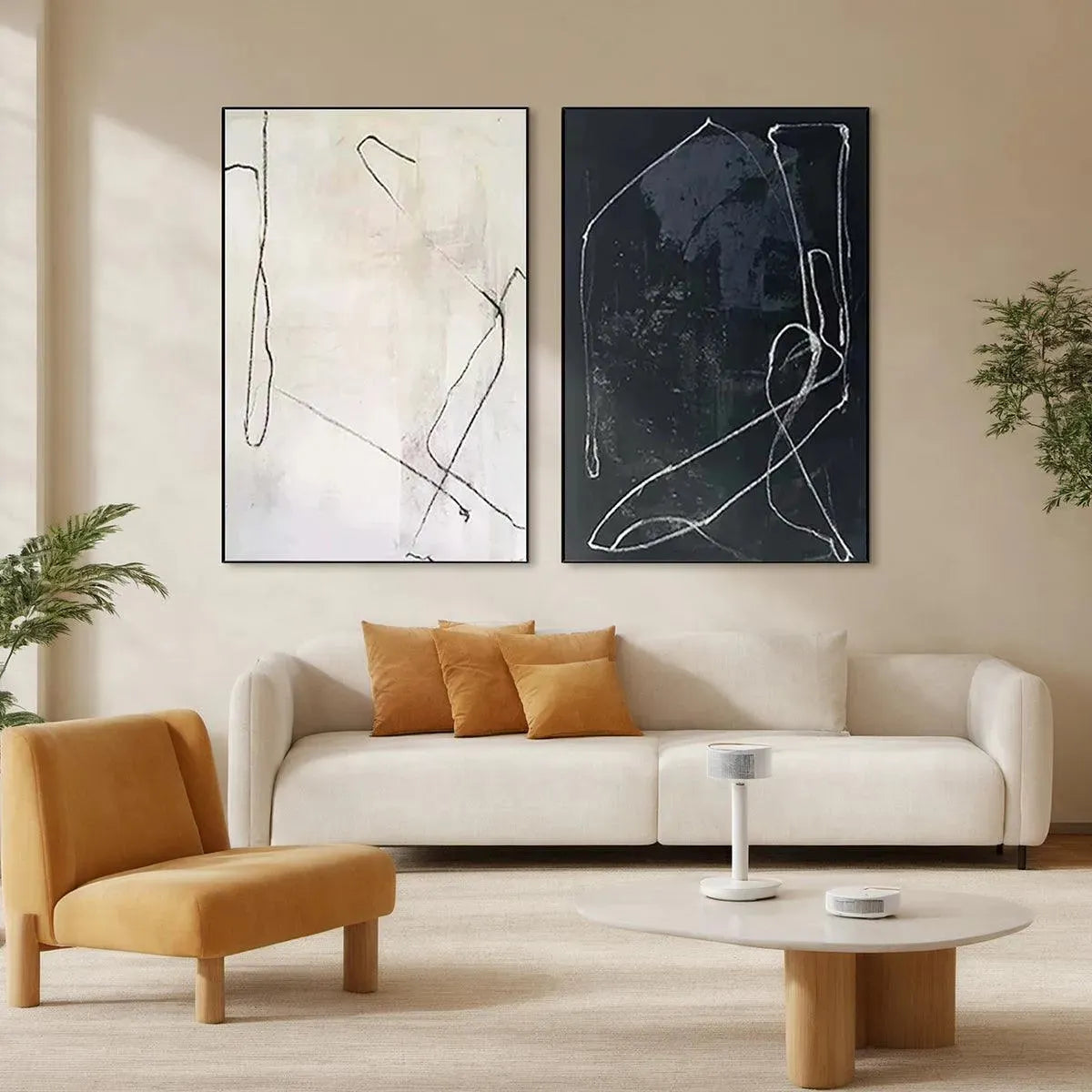 Minimalist Abstract Duo: black and white line art paintings in black frames above cream sofa with mustard pillows