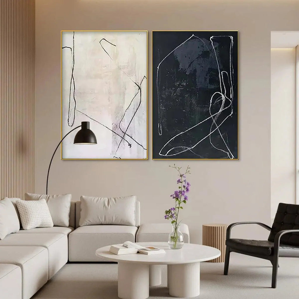 Minimalist Abstract Duo paintings in gold frames, white line art on cream and charcoal backgrounds, styled in a living room.