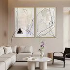 Set of 2 minimalist beige abstract paintings with black gestural lines, displayed in a modern living room.