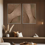 Set of 2 framed brown textured abstract paintings with curved designs in a modern living room setting.