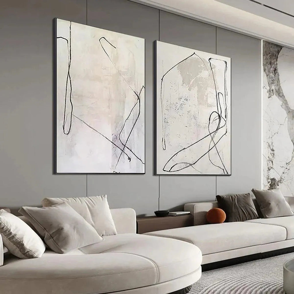 Two beige abstract paintings with black organic lines above a modern sofa in a living room.