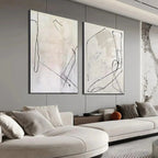 Two beige abstract paintings with black organic lines above a modern sofa in a living room.