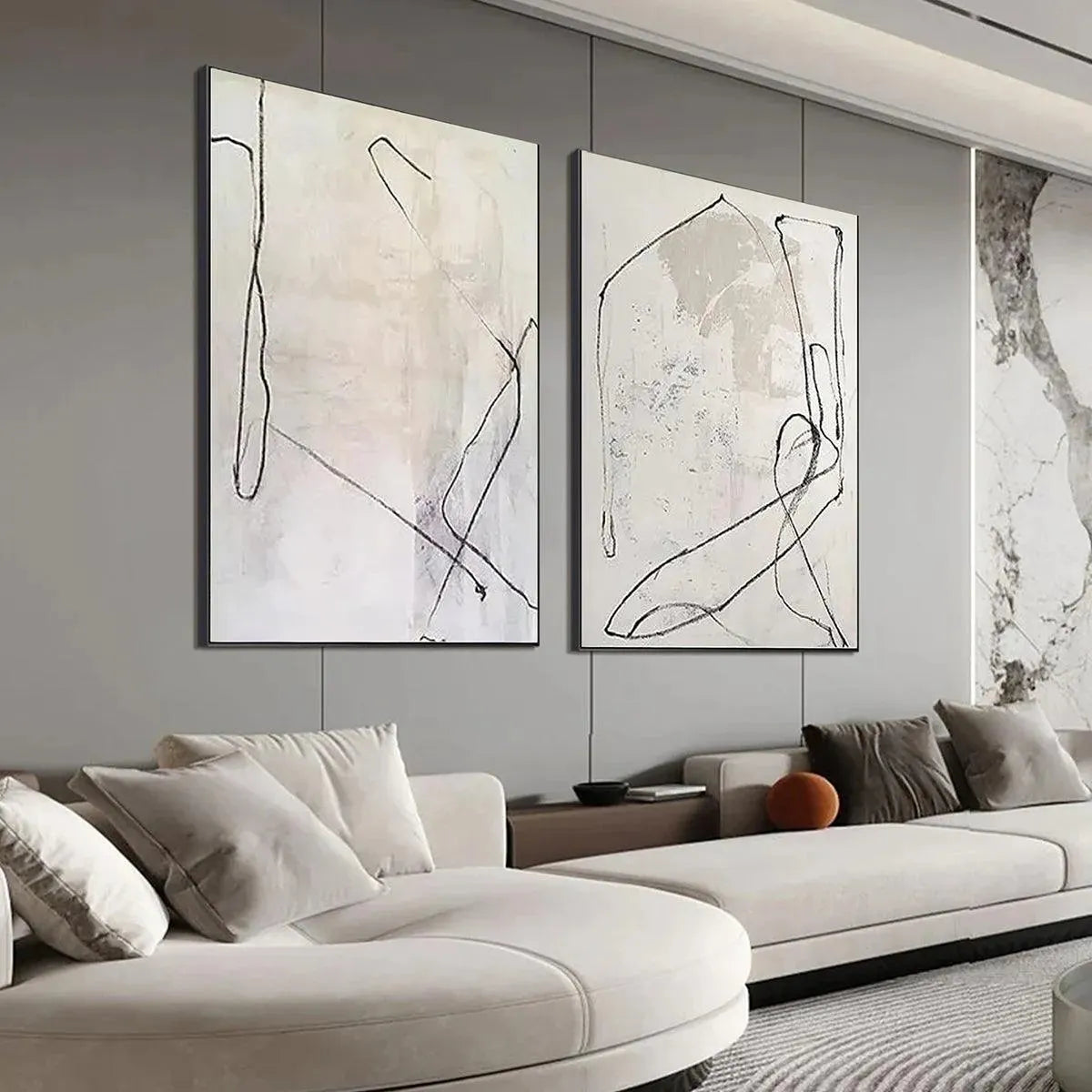 Two beige abstract paintings with black organic lines above a modern sofa in a living room.
