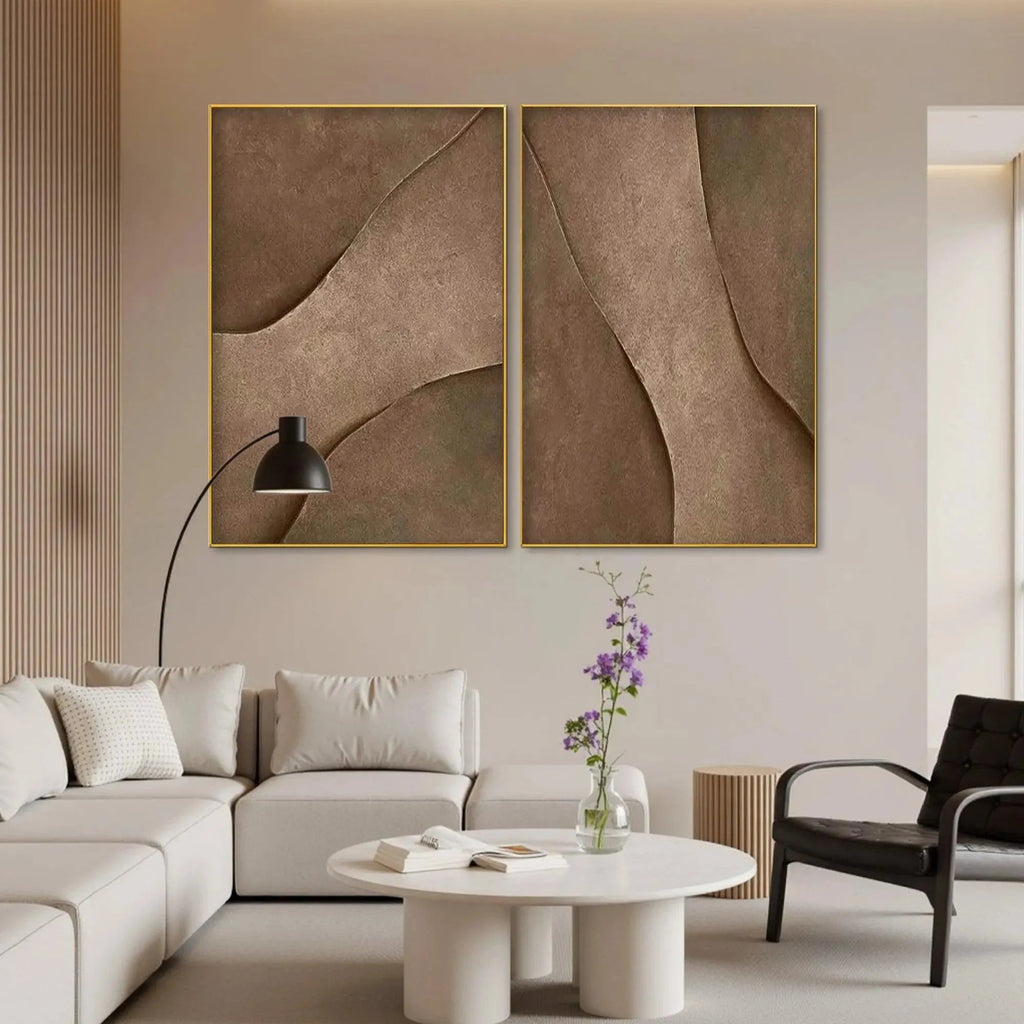 Set of 2 framed brown abstract paintings with textured organic lines above white sofa in a minimalist living room