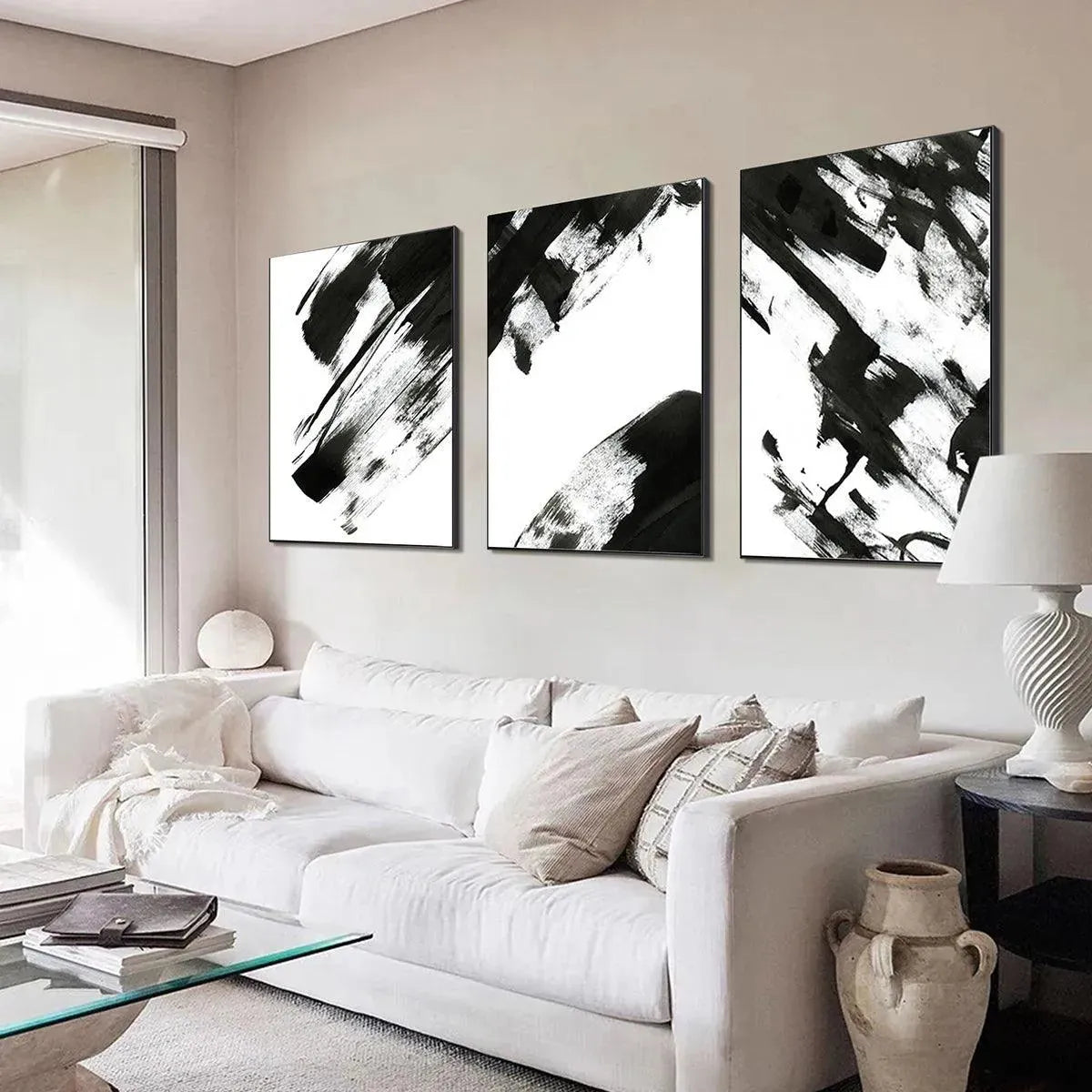 Black and white abstract triptych wall art set with bold brushstrokes above a white sofa in a modern living room.