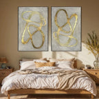 Two vertical abstract paintings with textured gray backgrounds and bold raised gold lines, displayed above a wooden bed.