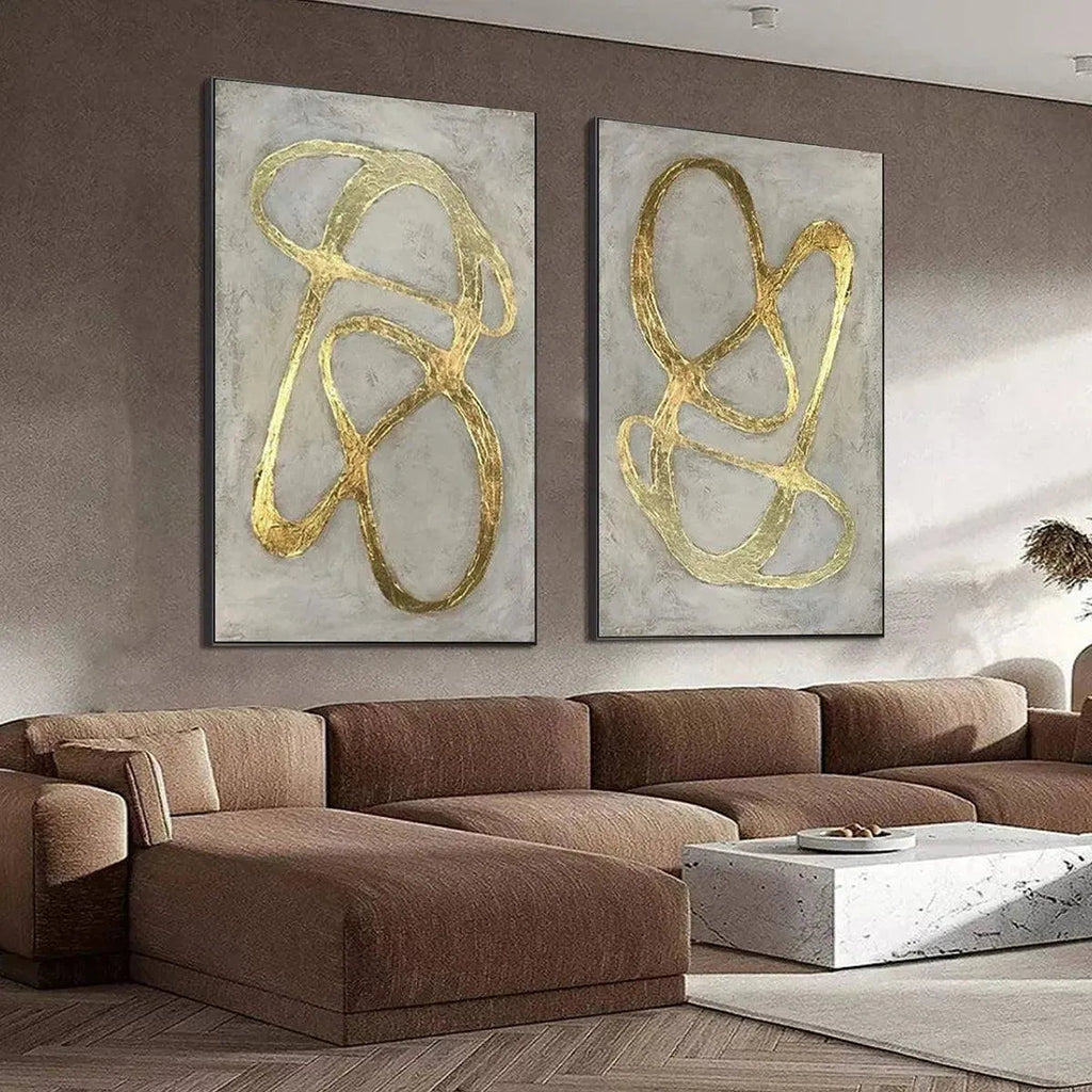 Two vertical abstract paintings, gray textured background with raised gold lines, black frame, above sectional sofa.