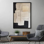 Framed beige and black abstract painting by Javier Ramirez in a modern living room with grey chairs.